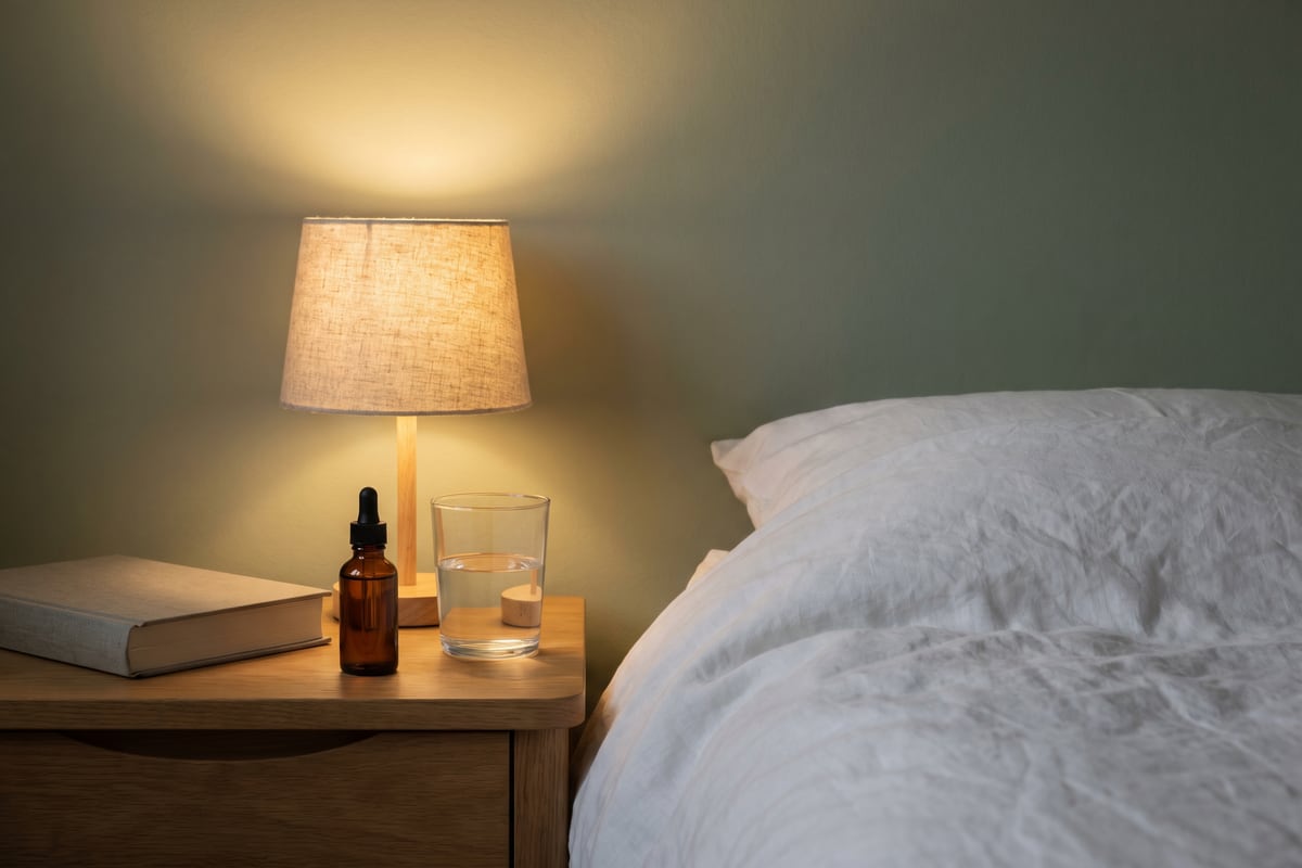 A bedside table with a lamp, a book, water and a small amber bottle